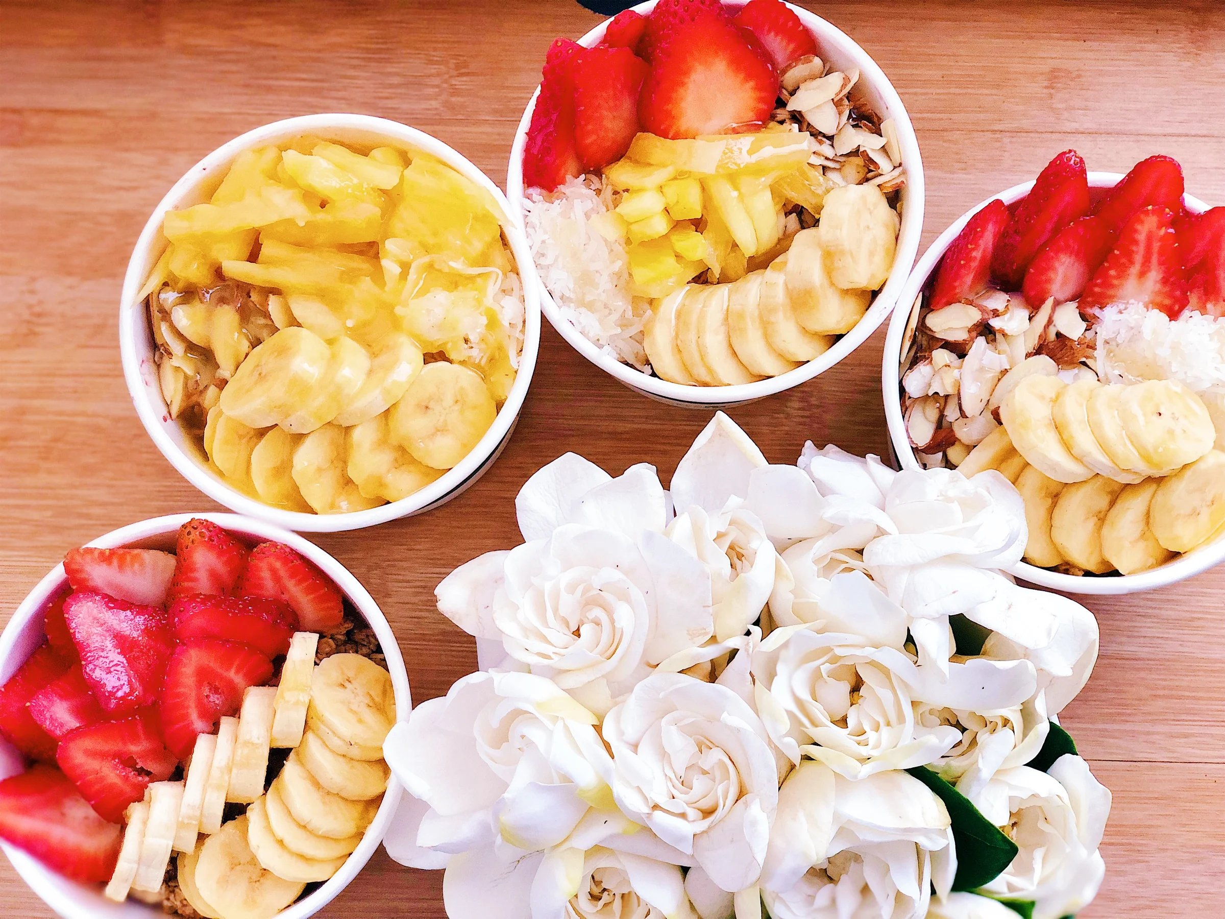 Four açaí bowls arranged with white gardenia flowers